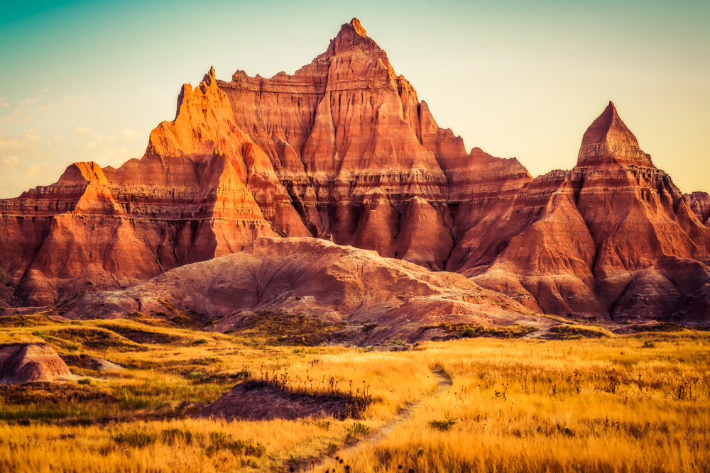 A view of a large rock formation that is made of red sandstone. There is also a prairie with tall grass. Its in Badlands National Park South Dakota. 