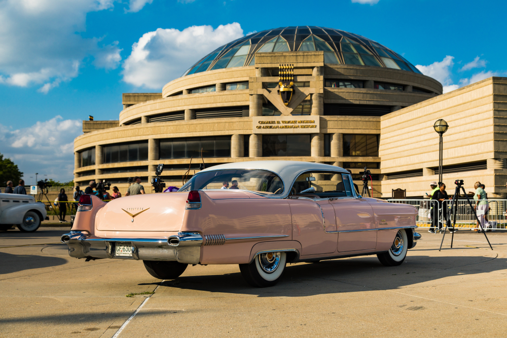 The exterior of a brown stone building that is the Charles H. Wright Museum of African American History. In front of it is a vintage pink Cadillac. Its one of the best things to do in Detroit. 