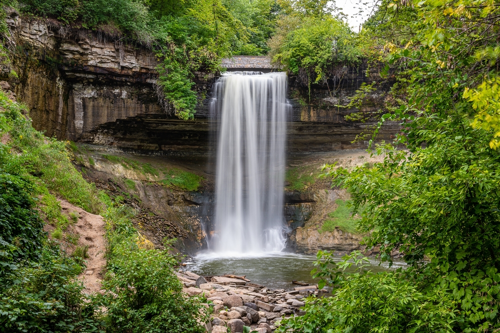 A waterfall flowing over the rock surrounded by vegetation. Visiting Minnehaha Falls is one of the things to do in Minneapolis