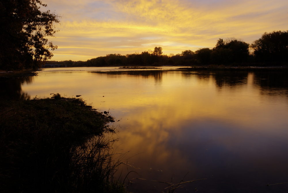 A sunrise over a lake with trees all around it.