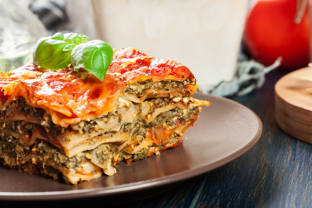 A vegetarian lasagna on a brown ceramic plate. On top of the slice of lasagna there is a sprig of fresh basil. Its similar to a dish you can find in restaurants in Detroit.