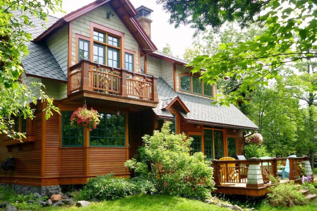 One of the largest cabins in Minnesota has brown wooden exterior with flowering plants and lush landscaping.