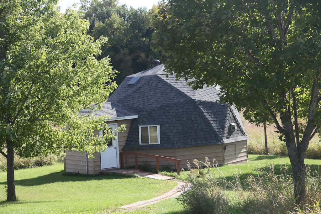 Dome cabin with gray roof surrounded by grass and trees.