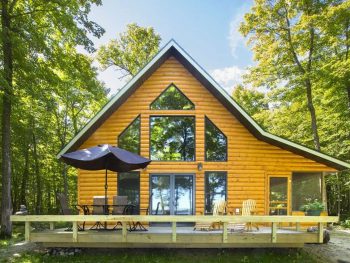 Cabin in Minnesota with brown exterior and black trim. Black patio furniture and umbrella for shade on patio