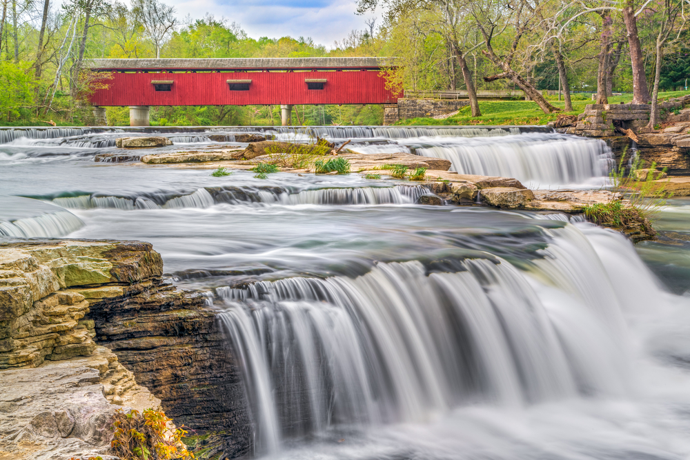 A waterfall with a red covered bridge in the background.