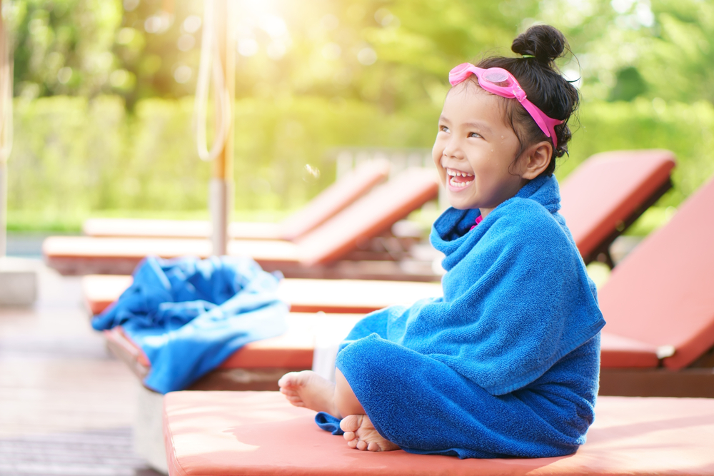 A young girl wrapped in a towel on a lounge chair.