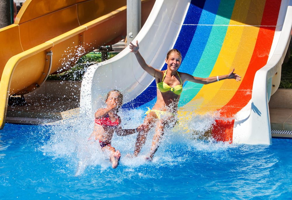 Two kids landing in a pool at the bottom of a rainbow waterslide.