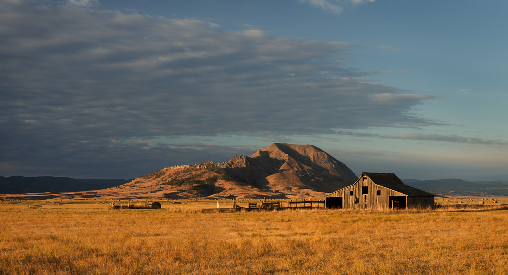 A view of Bear Butte, a small mountain surrounded by prairie lands in SD. In front of it, in the prairie, is an old barn. It is one of the best state parks in South Dakota. 
