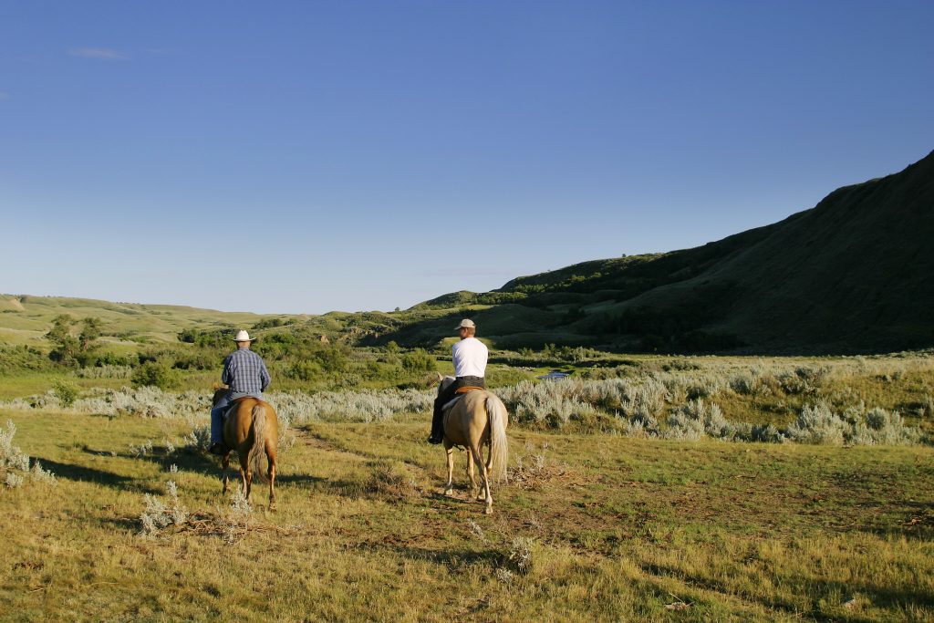Two men riding horses in a prairie at a state park in South Dakota. 
