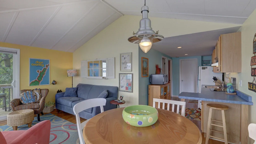 The bright airy inside of the boathouse with a yellow wall, blue sofa and a wooden table.