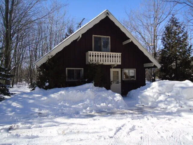 A brown cabin in the snow with trees behind it. Cabins in Door County
