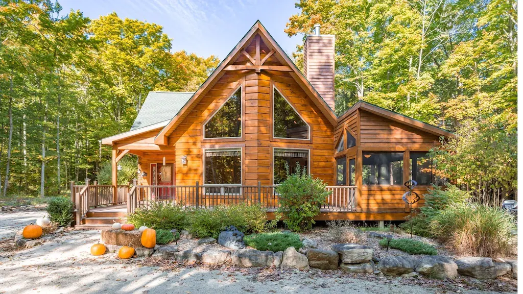 A large log cabin with large window and a front yard with trees behind