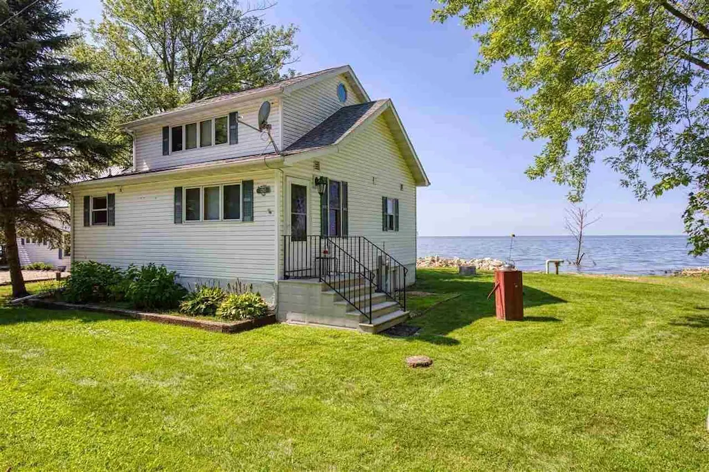 A white cottage on the water with a grass yard in an article about cabins in Door County