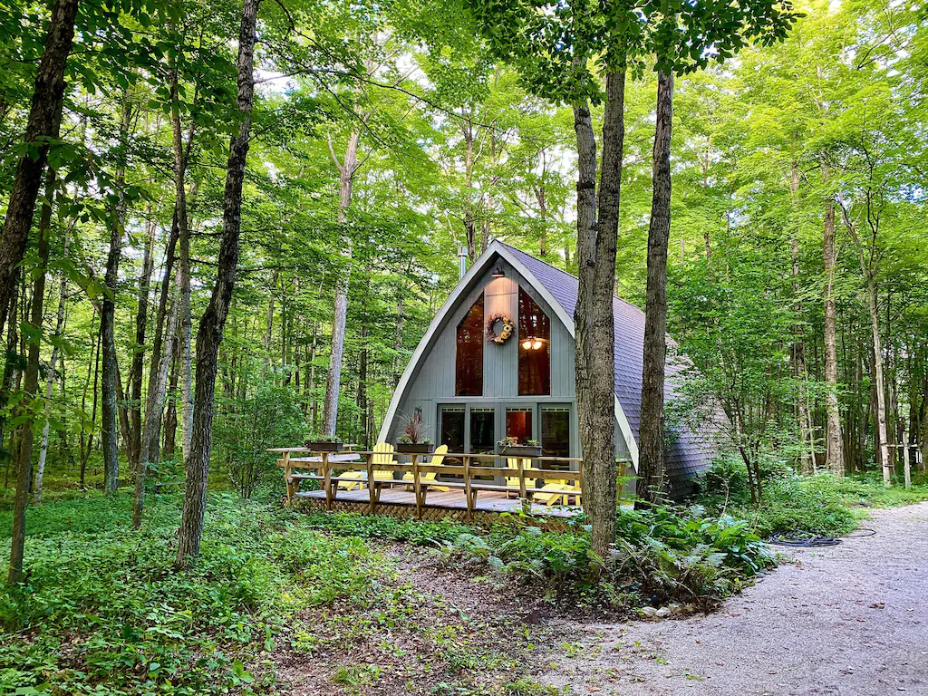 A grey cabin in the woods with a large porch