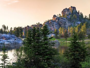 One of the amazing views at Custer State Park in South Dakota. There is a large mountain rock formation, a lake, grassy areas, tall trees, and more.