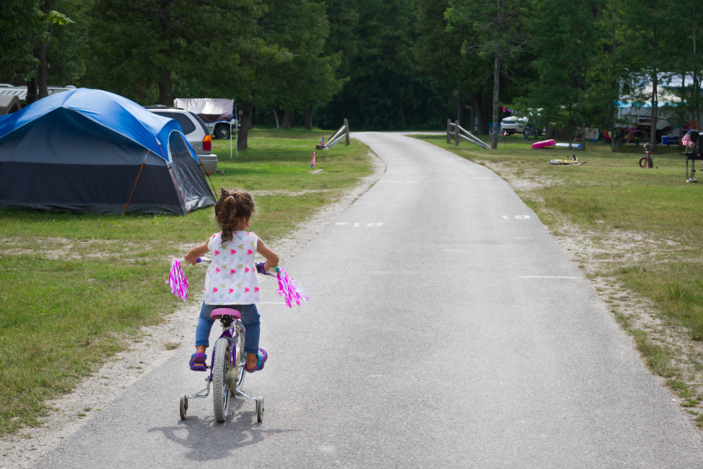 A child riding a bike through a family camping ground in Michigan. You can see other tents, bikes, and families outside. 