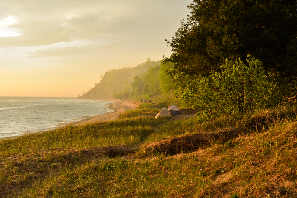 Tents set up on the shore of Manitou Island, one of the best places for camping in Michigan. The sun is setting and the sky has a yellow haze to it.