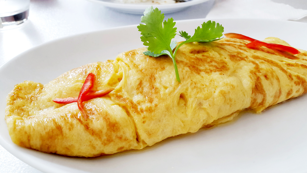Close up of an omelet on a white plate with a garnish