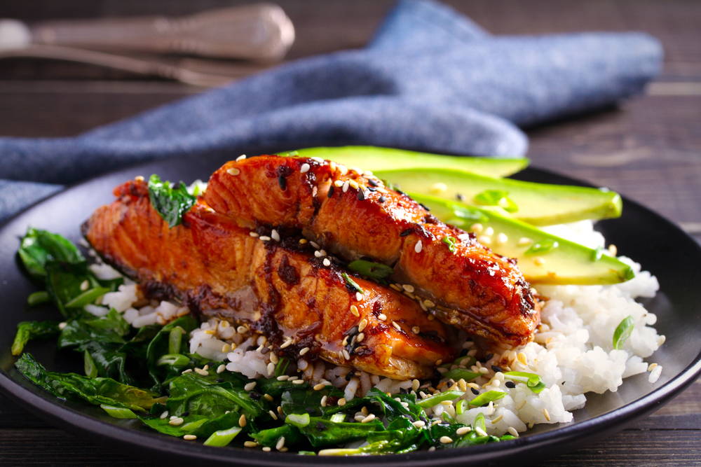Salmon with rice and greens and avocado covered in sauce