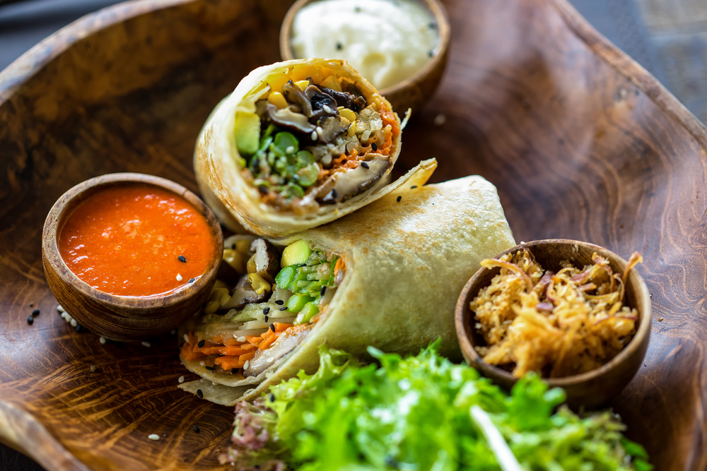 A vegetarian wrap with a side f sauce in a wooden bowl in an article about restaurants in Kalamazoo