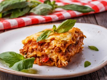 Lasagna on a plate with a red and white napkin in the background