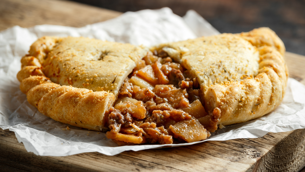 A pasty with meat and vegetables split open on a piece of paper