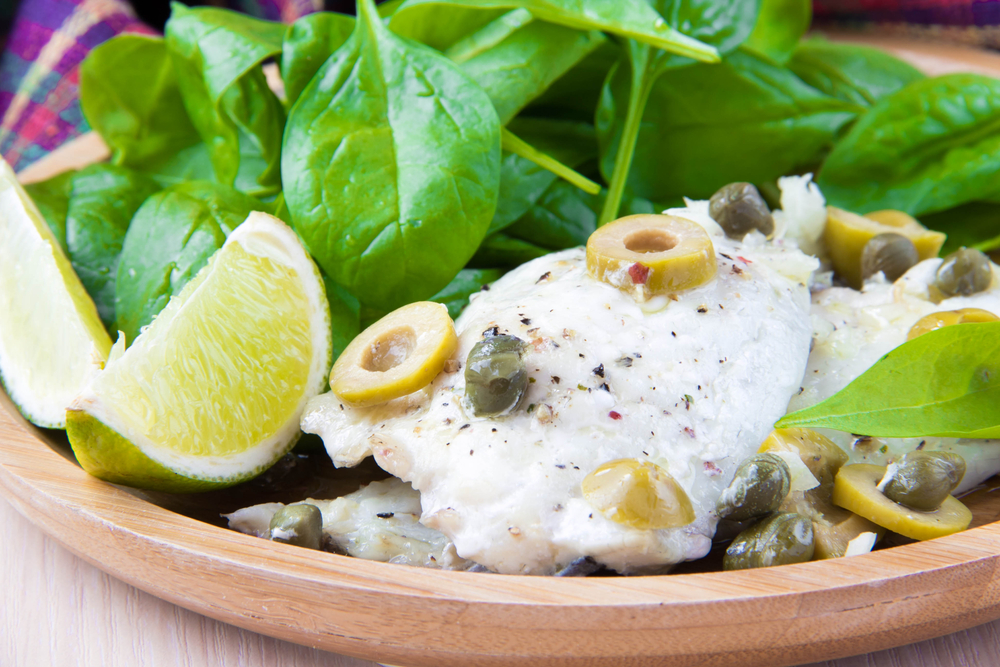 White fish with capers and spinach on a wooden plate