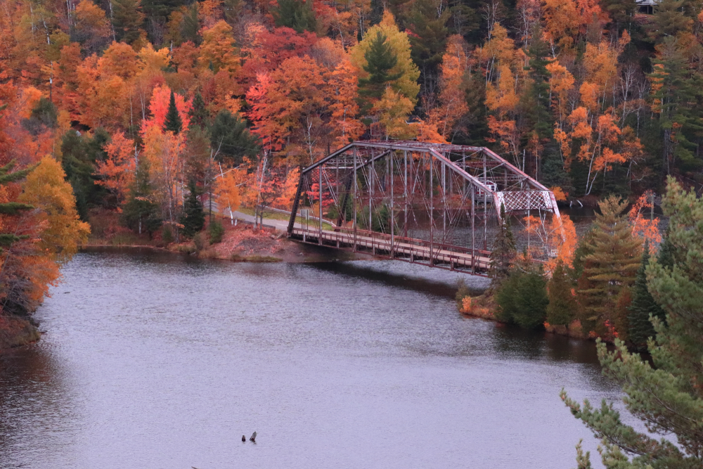 An iron bridge crossing the river in a valley surrounded by autumn foliage