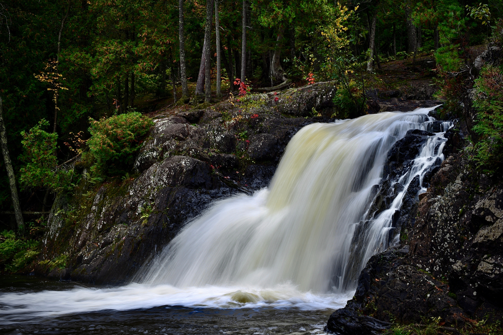 Dead River Waterfall flowing over the rocks with trees in the background in an article about things to do in Marquette MI