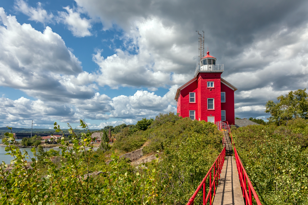 A red lighthouse at the end of a wooden boardwalk surrounded by greenery
