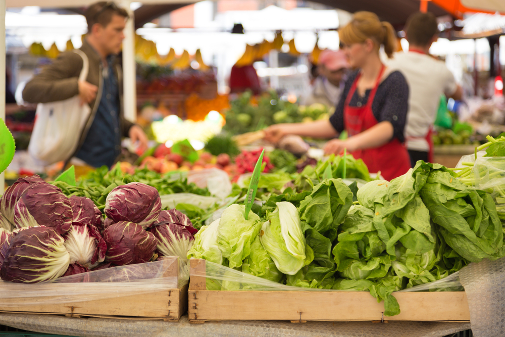 A Farmer Market with produce in the foreground and people working in the background