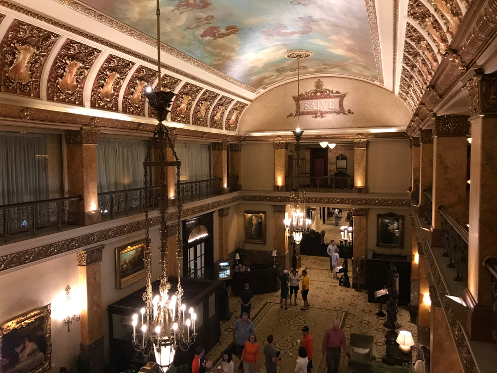 The inside of a grand hotel with a painted ceiling and molding with people in the lobby