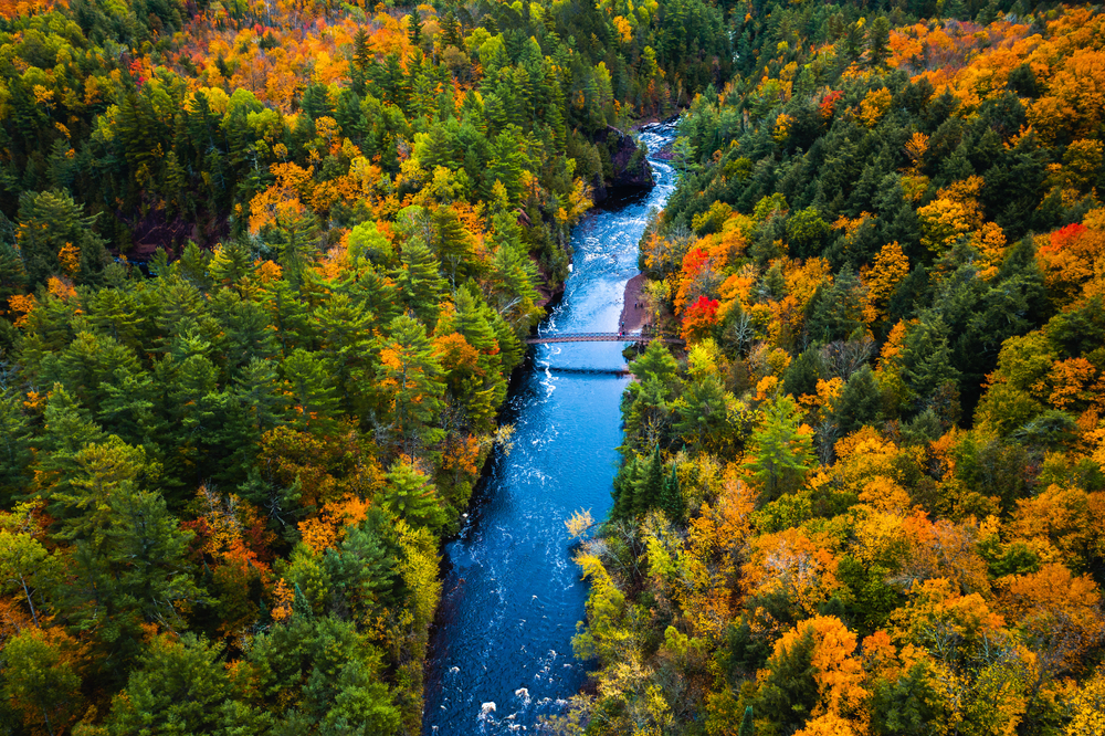 Aerial view of a bright, blue river cutting through the fiery foliage of Copper Falls State Park, one of the best places to visit in Wisconsin in fall.