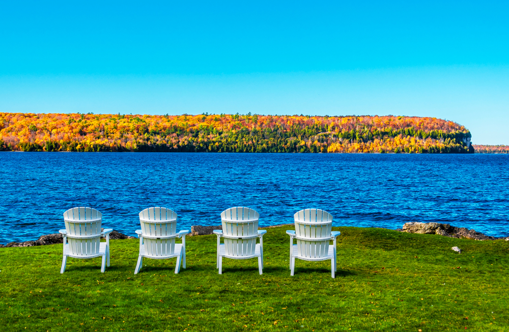 Four white, outdoor chairs lined up next to the lake in Door County, one of the best places to visit in Wisconsin.