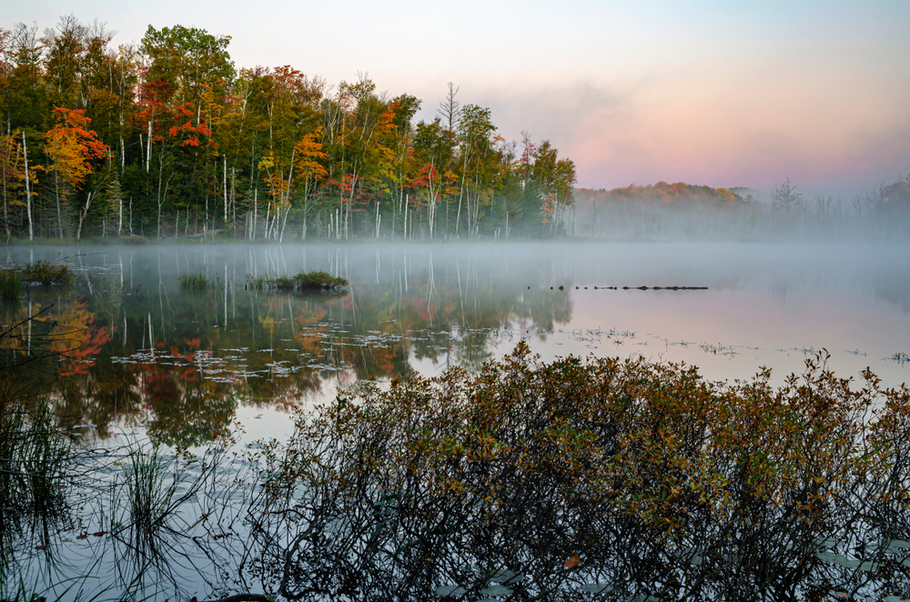 A misty morning over a lake in the Hiawatha National Forest. with colorful fall foliage one of the spectacular places to visit in MI