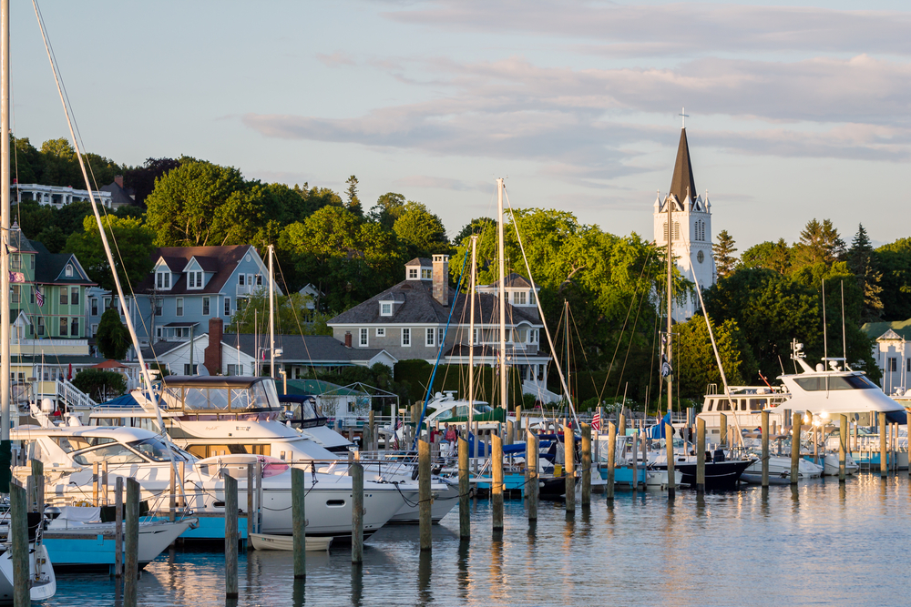The marina on Mackinac Island full of sailboats with a church and trees in the distance.