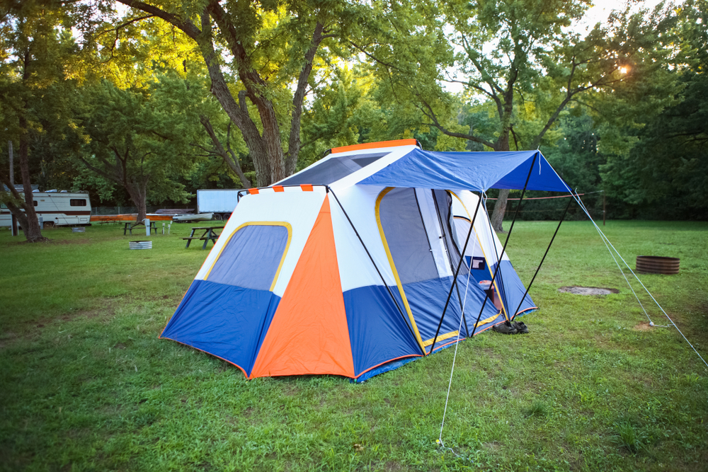 A blue, white, and orange tent in the middle of a grassy area that is a campsite for camping in Ohio. There are some trees around the area. 