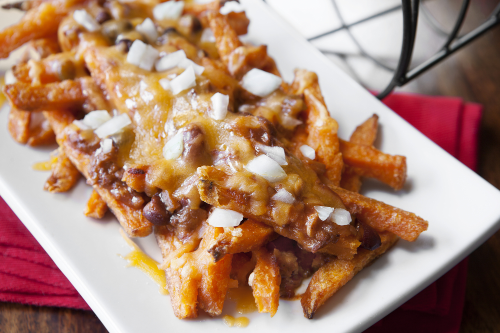 A long white plate piled with chili cheese fries with fresh chopped onion on top. 