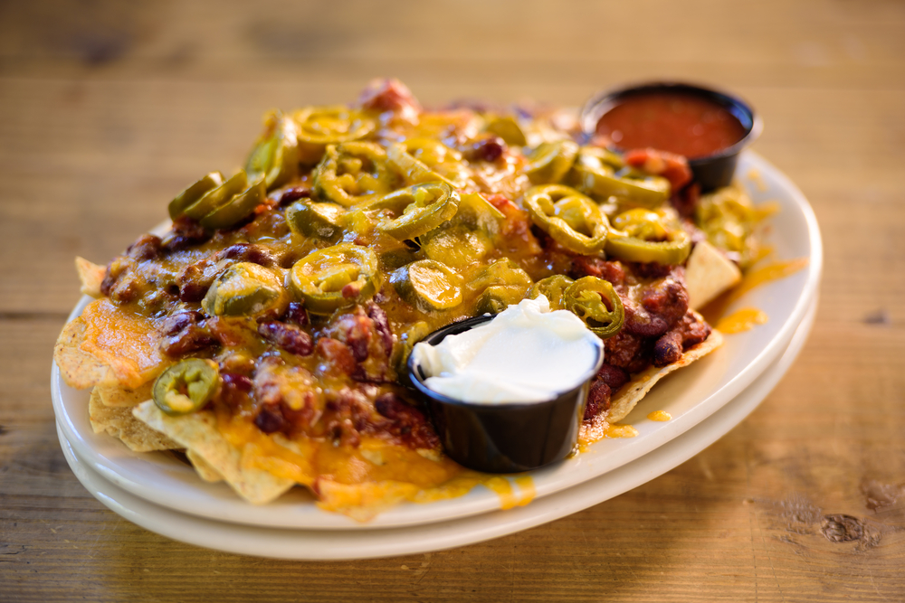 Loaded nachos with cheese, chili, and cheese with source cream and salsa sauce pots