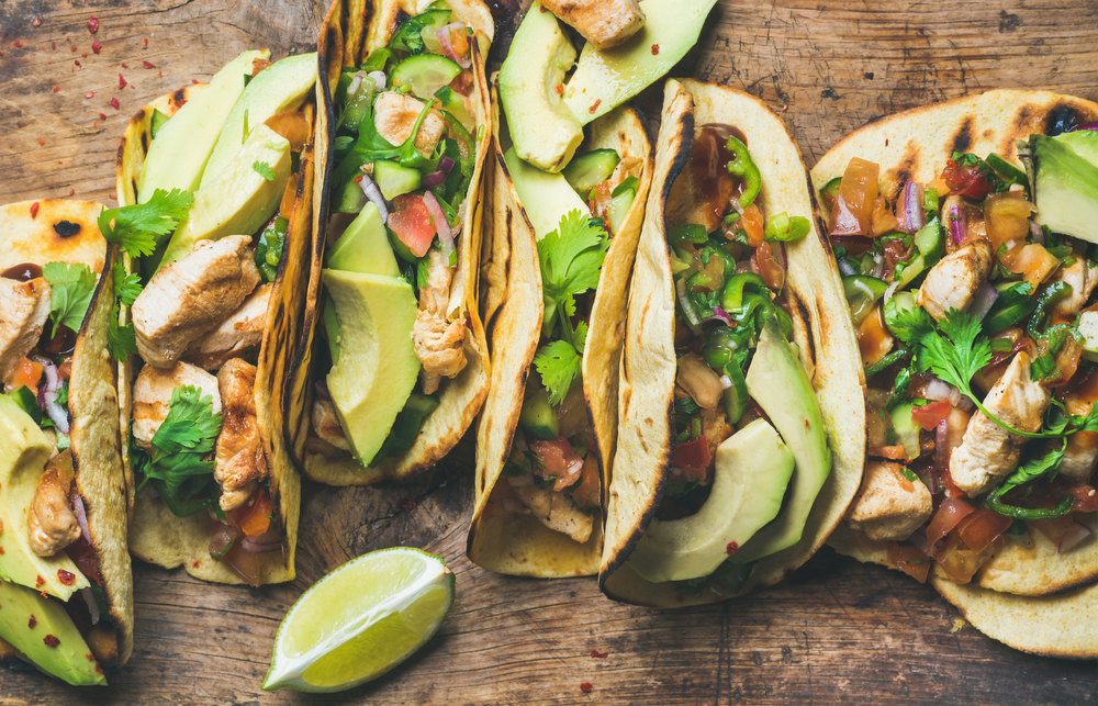 Soft Tacos filled with chicken, avocado and salad on a wooden board with a lime on the side