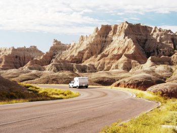 An RV driving down the road through the rock formations in Badlands National Park. One of the best places for camping in South Dakota