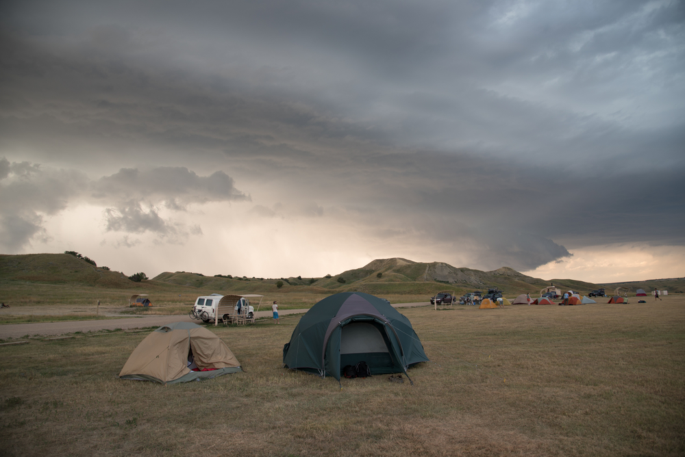 Tents and campervans in a grassy field near the Black Hills on a cloudy day. 