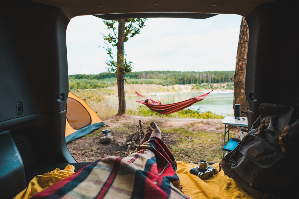 Looking out the back of a camper van towards a person in a hammock. In the background you can see a large lake. 