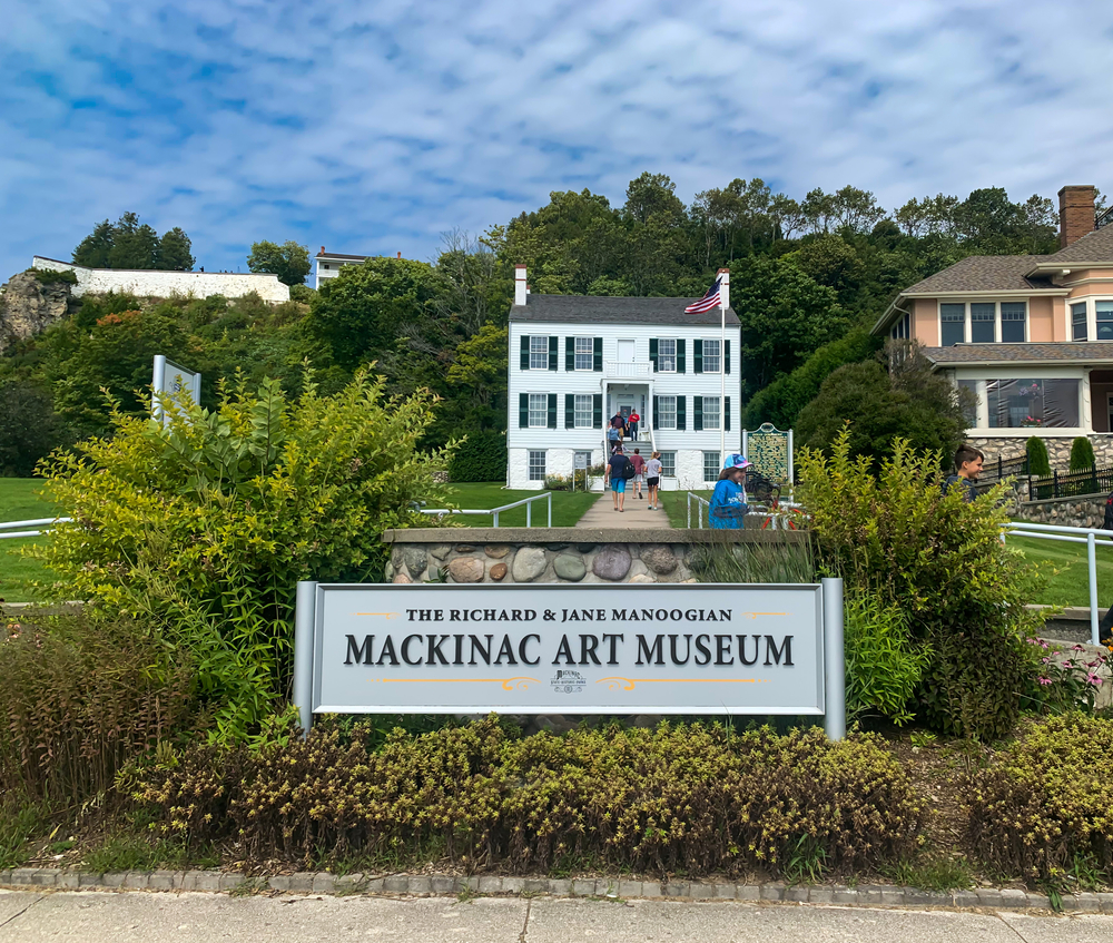 The sign for the Mackinac Art Museum in front of the little, white building.