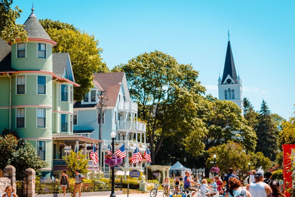 People walking and riding bikes next to old Victorian homes in downtown, one of the best things to do in Mackinac Island.