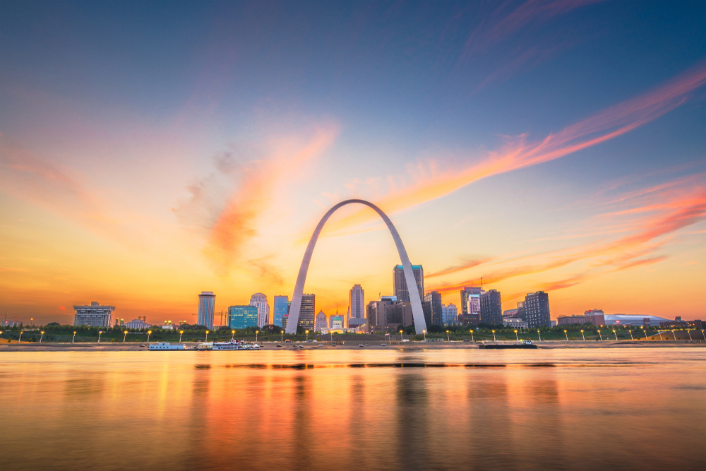 Skyline of St. Louis with the Gateway Arch in the center as seen from across the river at sunset. This is one of the most famous places to visit in Missouri.