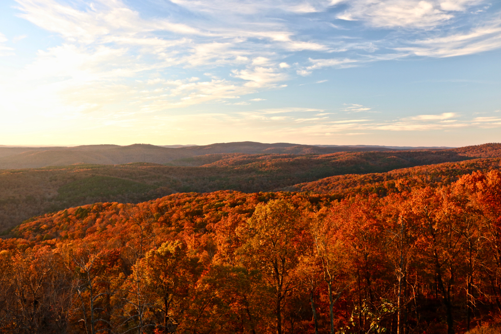 A golden sunset over the Ozark Mountains, which are red with fall foliage.
