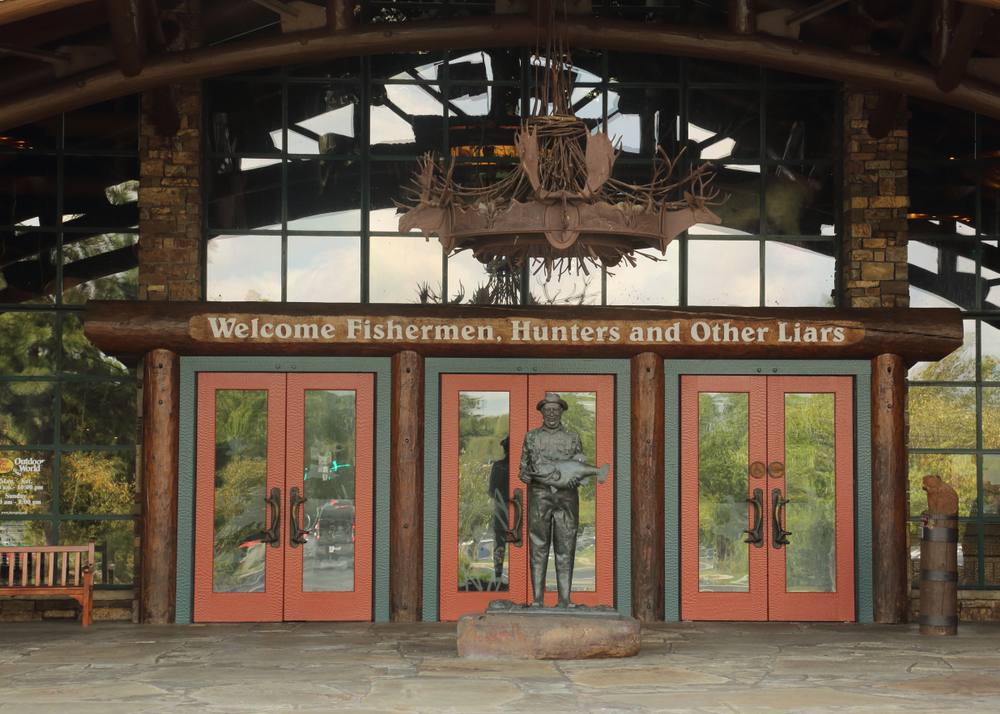 Entrance to Bass Pro Shops Outdoor World with the words "Welcome Fishermen, Hunters, and Other Liars" over the door and a stature of a man holding a fish.