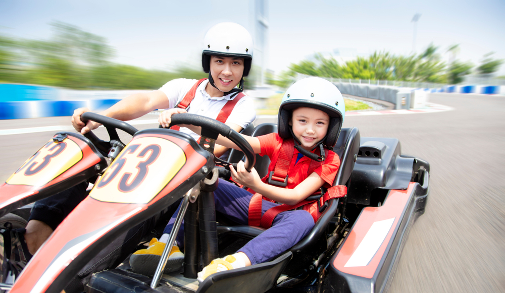 A man and a young child riding in go-karts on a track on a sunny day. 