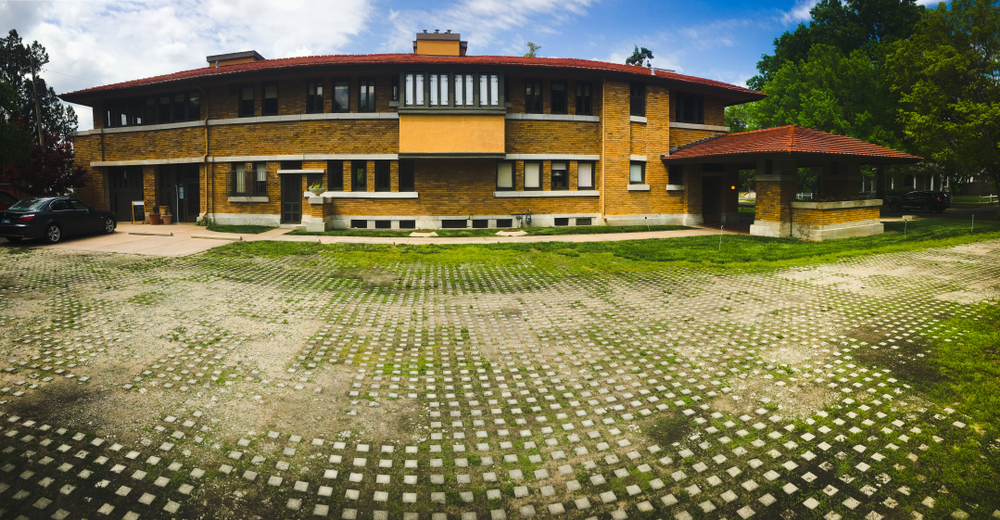 The exterior of the Allen House, a historic home designed by Frank Lloyd Wright. It is made of yellow and orange brick with red shingles. The yard has small stone squares in the grass. 